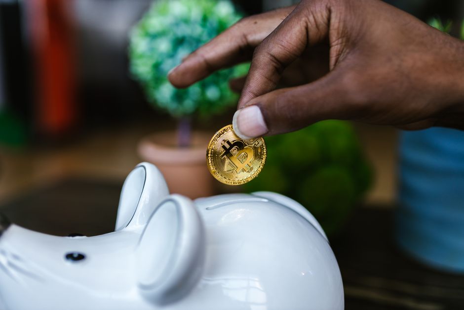 A close-up of a hand placing a bitcoin into a white piggy bank, symbolizing investment and