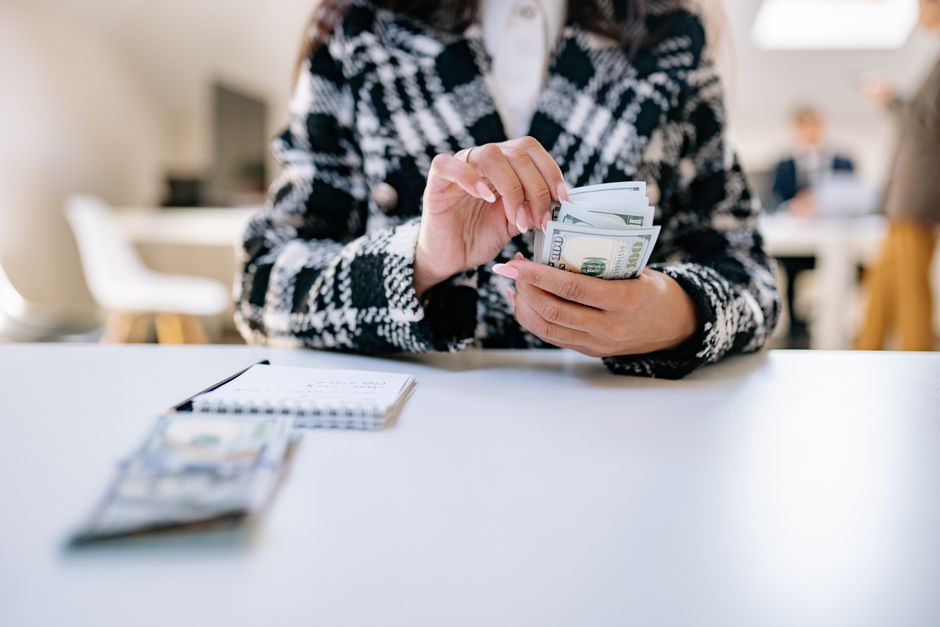 A close-up of a woman counting US dollars in an office environment, symbolizing financial 