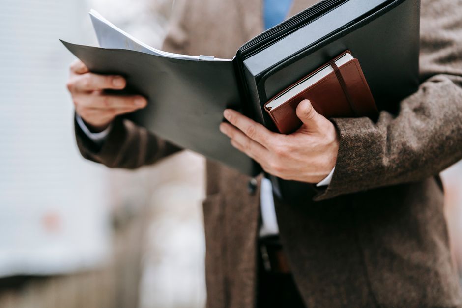 A professional in formal attire holding a notepad and folder outside, emphasizing business