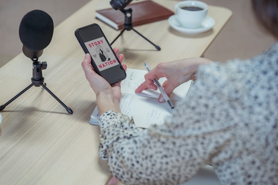 Back view faceless female in stylish blouse browsing mobile phone while sitting at desk with microphones and diary during interview