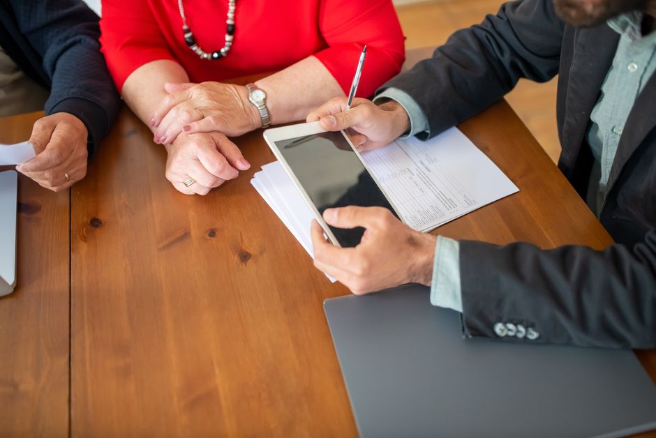 Business meeting at a wooden table with consultant reviewing documents and using a digital
