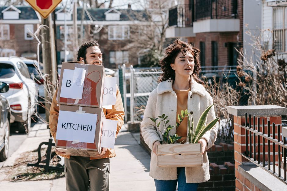 Happy couple carrying boxes and plants while relocating to a new city residence.