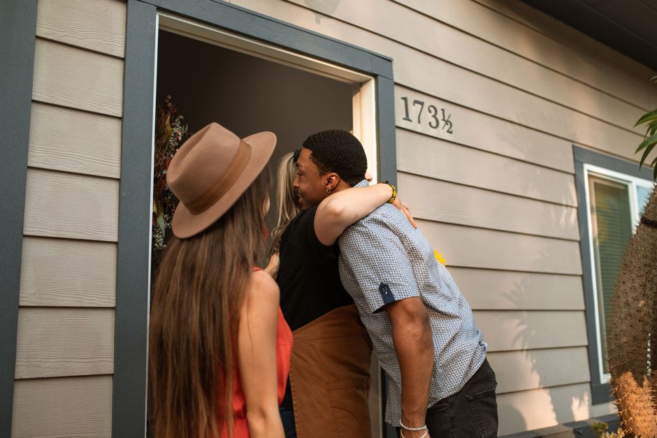 Three adults warmly embrace at a doorway, exuding friendship and connection.