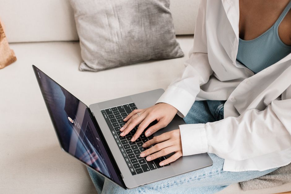 Casual scene of a woman typing on a laptop while sitting on a couch at home.