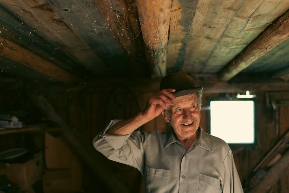 A joyful senior man smiling under a wooden hut's rustic ceiling.