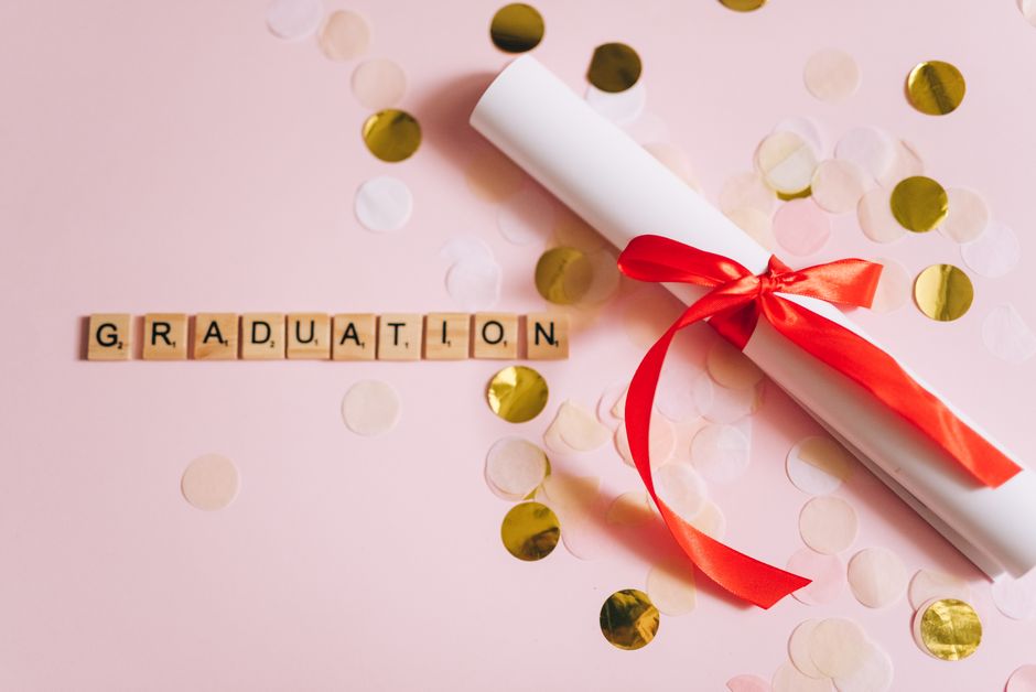 Flat lay of a graduation diploma with red ribbon and letter tiles spelling 'graduation' on