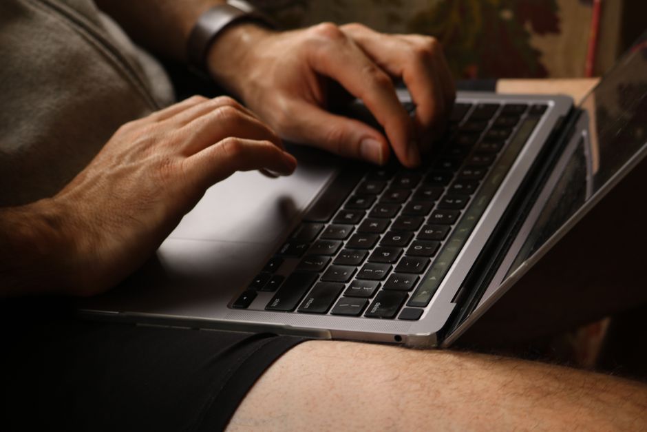 Typing on a laptop keyboard, close-up of hands in casual indoor setting.