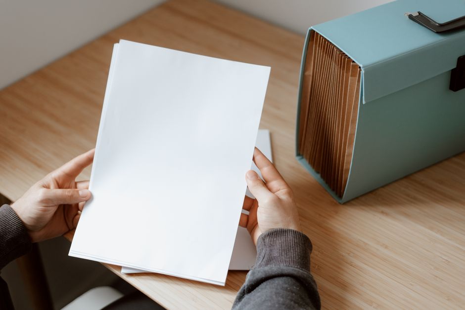 From above of crop unrecognizable person selecting sheet of paper against briefcase for do