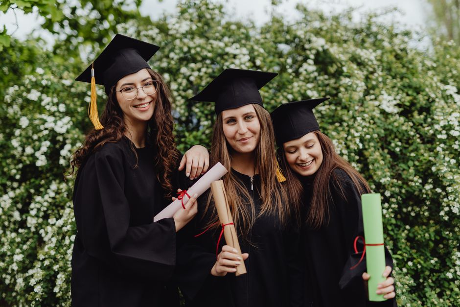 Group of smiling young women graduates posing with diplomas outdoors.