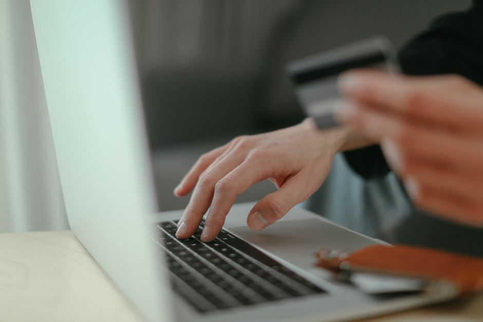 Close-up of hands holding a credit card and typing on a laptop keyboard for online shopping.