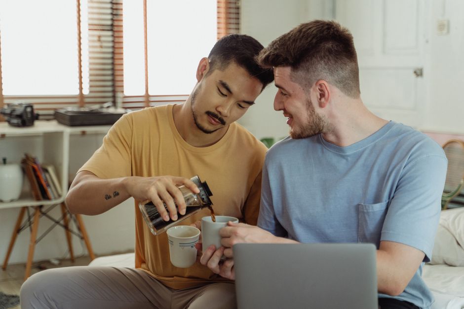 Loving same-sex couple enjoys morning coffee indoors, embracing togetherness.