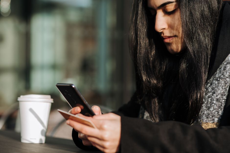 Side view of crop young Hispanic female purchaser shopping online on cellphone with plasti