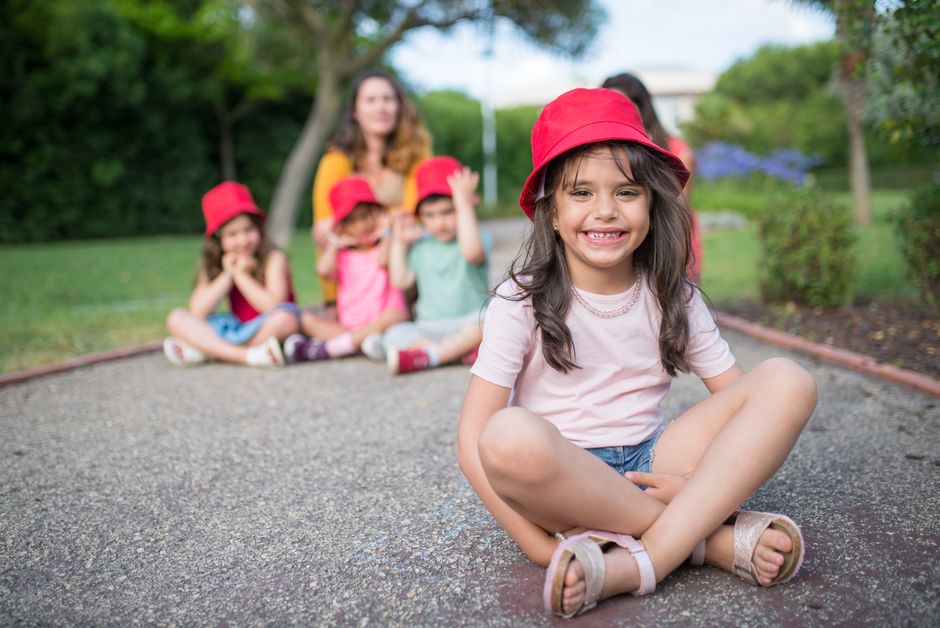 A cheerful young girl sits outdoors with friends, all wearing red hats. Perfect for youth and friendship themes.