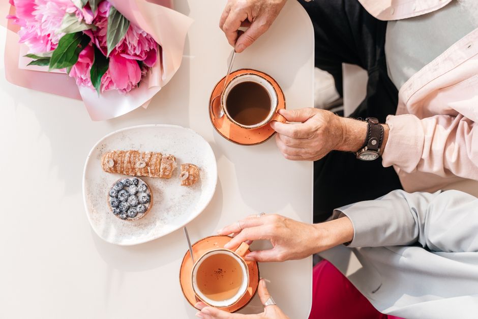 Top view of two people enjoying coffee and pastries at a table adorned with flowers.