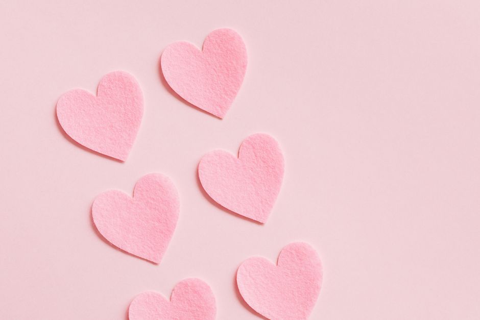 From above romantic composition of heart shaped uneven paper cutouts placed diagonally in lines on pink surface love concept