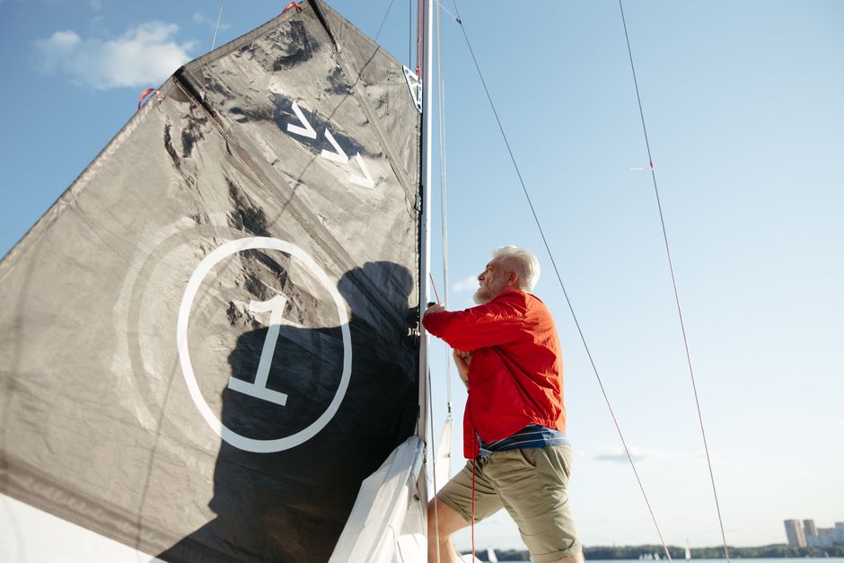 Elderly man in orange jacket enjoying a sunny day sailing on the sea.