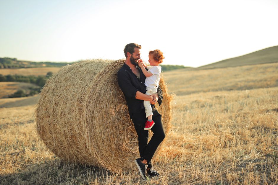 A father and child bonding outdoors by a hay bale on a sunny summer day.