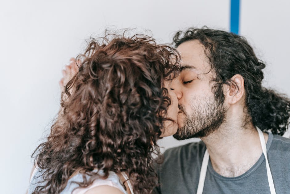 A young couple shares a tender kiss indoors, showcasing romance and love in a relaxed setting.