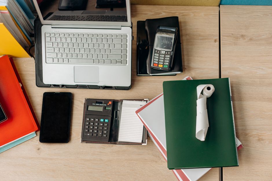 An organized office desk featuring a laptop, calculator, payment terminal, and documents.